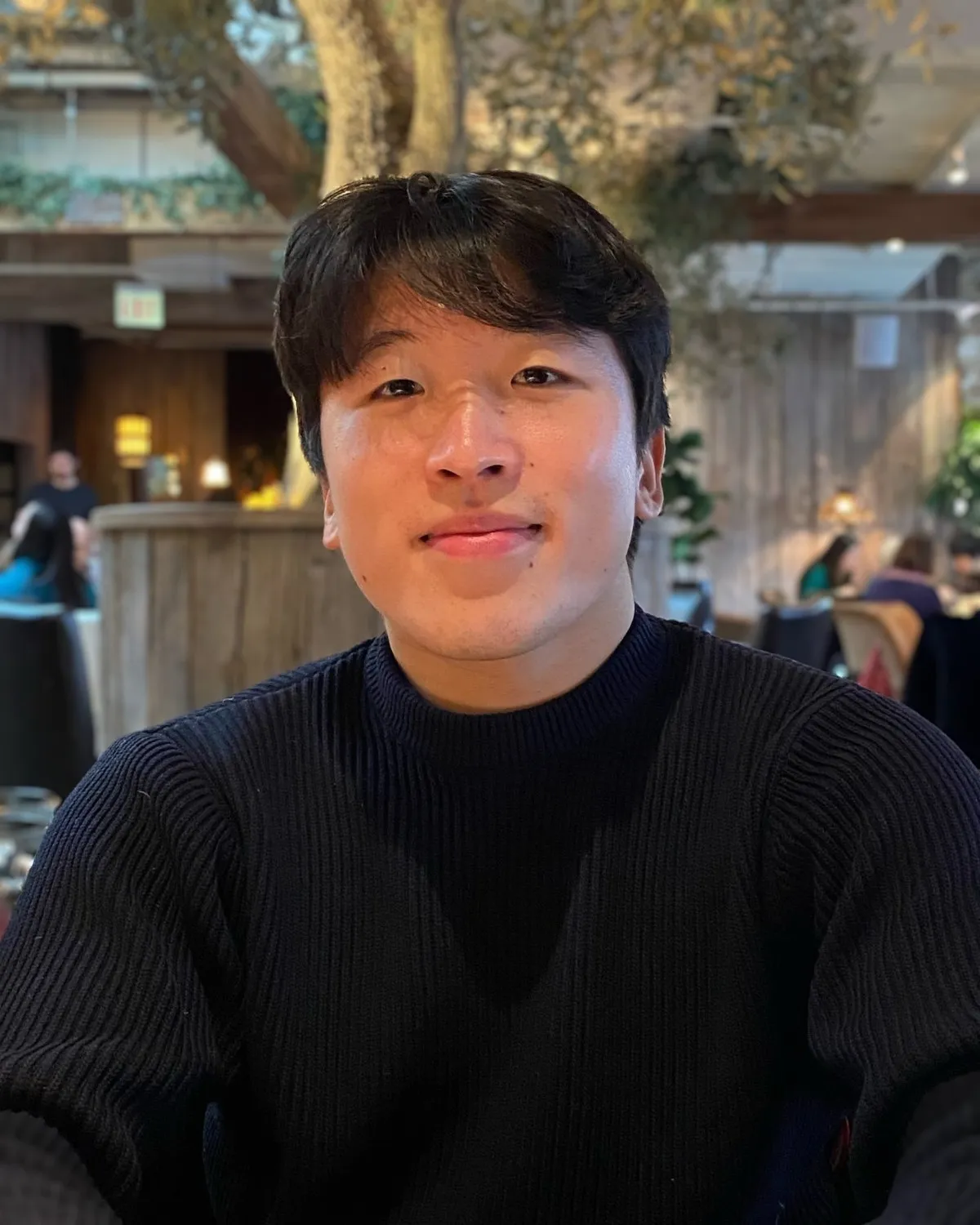 Zachary Kim, founder of Arc Systems, smiling at a restaurant table under an olive tree